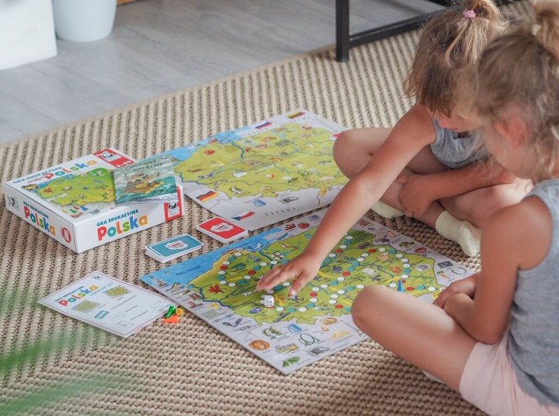 Dziewczynki grają w grę edukacyjną Polska na planszy z mapą kraju, zabytkami i przyrodą